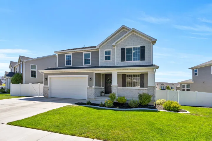 Two-story residence featuring a gray and light-gray shingle and siding exterior, a white two-car garage, a covered front porch, and a stone facade foundation