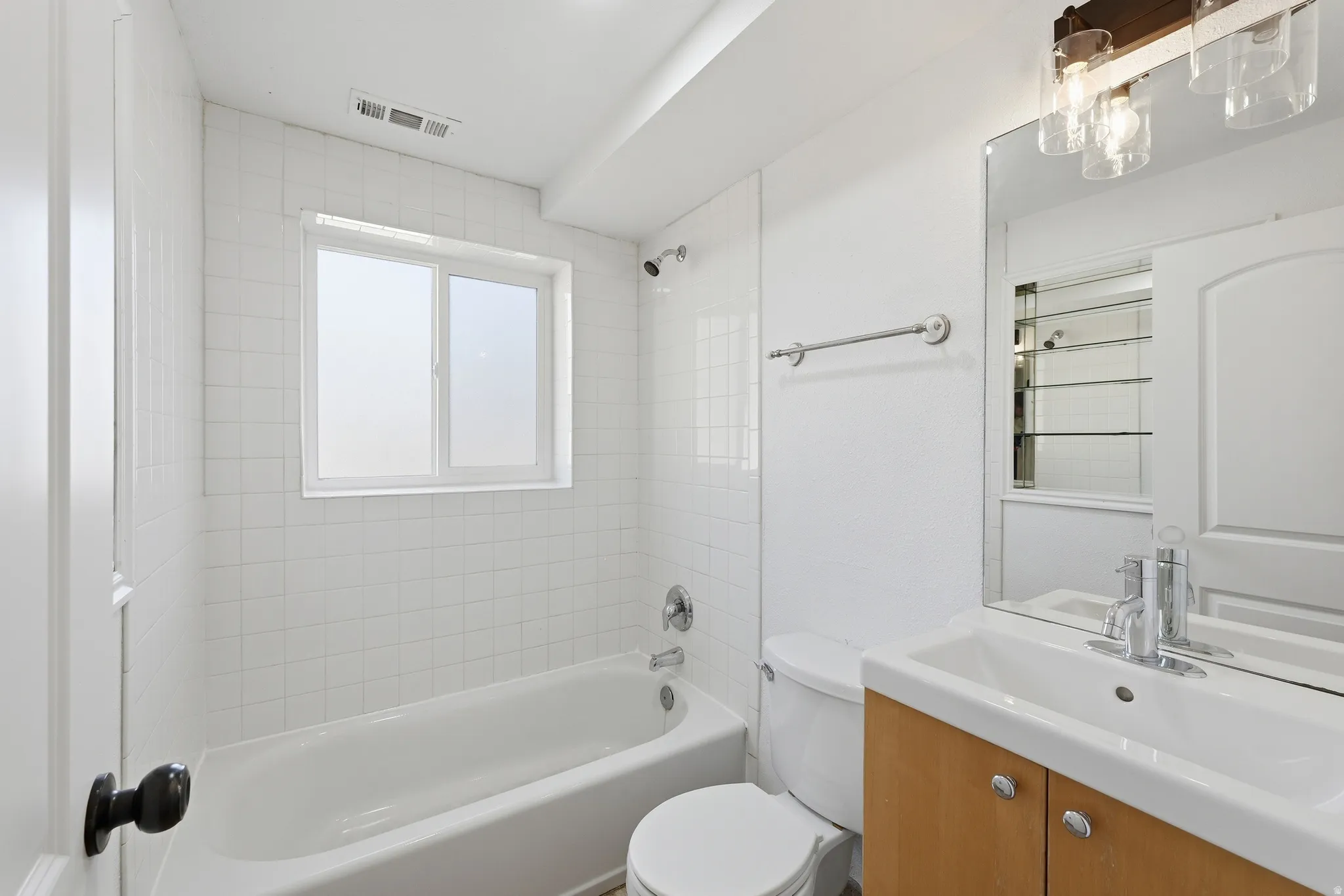 Bathroom featuring a white subway tile surround, a built-in tub with shower, a window with frosted glass, a toilet, and a vanity with an integrated sink