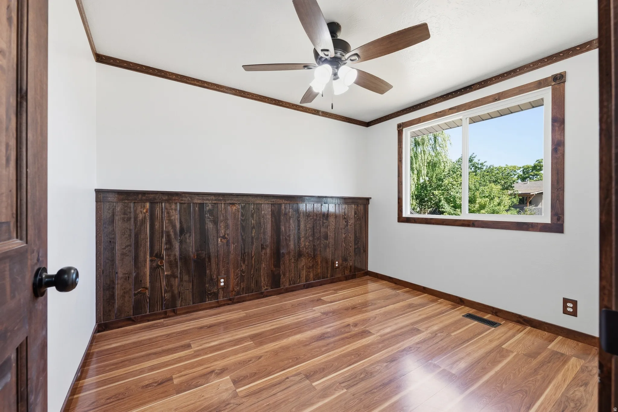 Spacious room featuring wood-finish flooring, half-wall wood paneling, and a ceiling fan with light fixture
