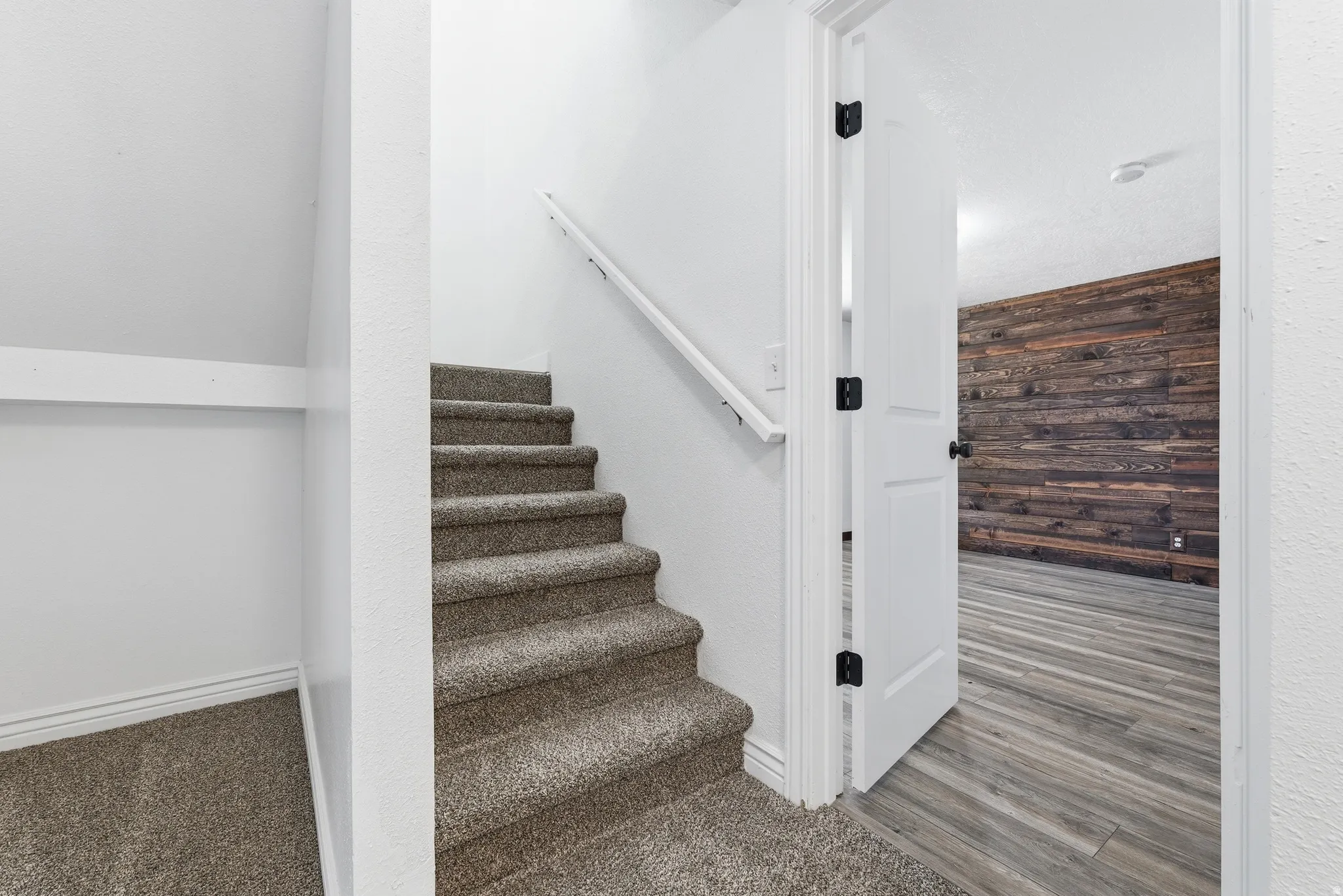 Carpeted stairs with a white handrail, leading down to a room featuring wood-finish flooring and a horizontal wood plank accent wall