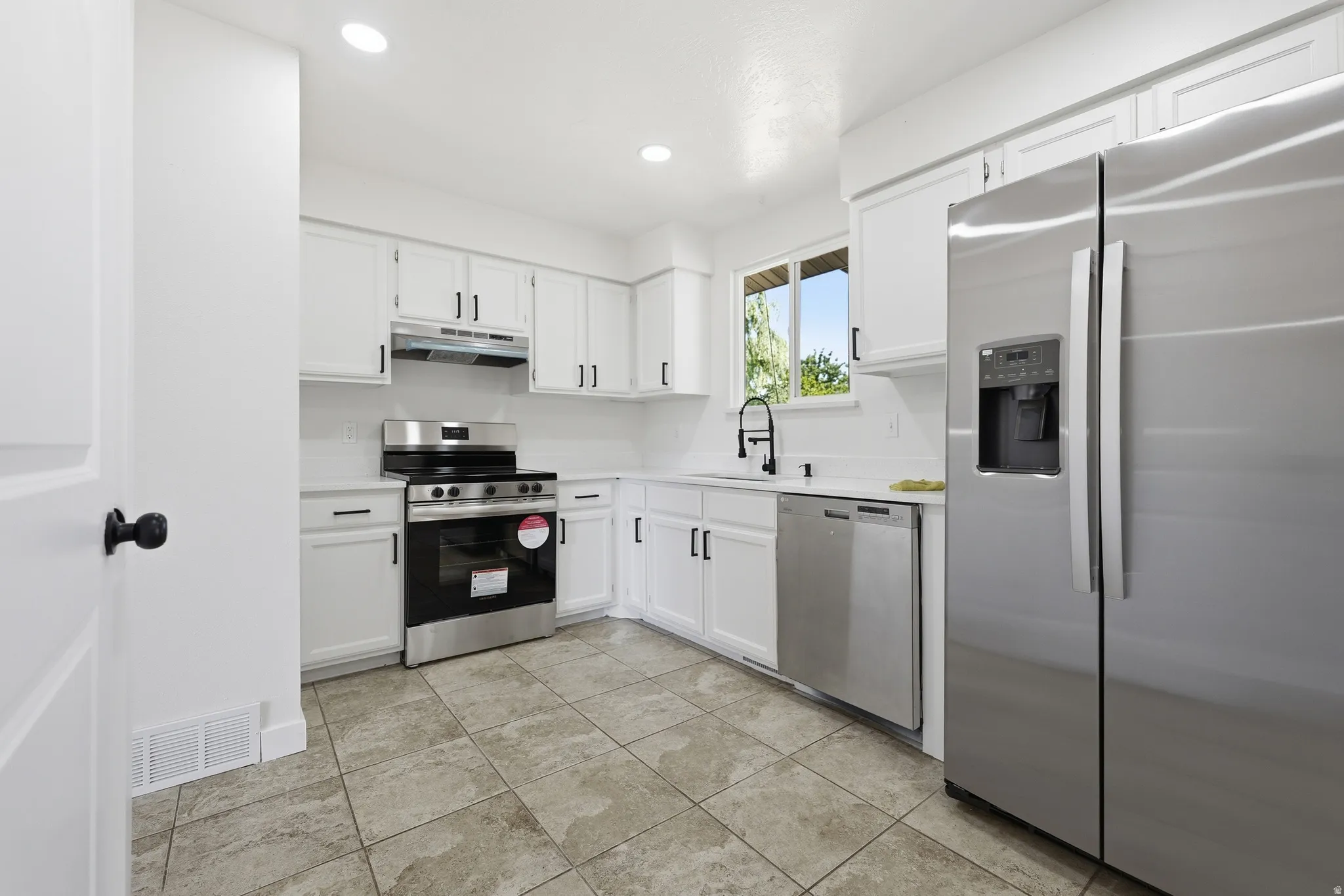 Kitchen featuring white cabinetry, stainless steel appliances, tile flooring, recessed lighting, and a window