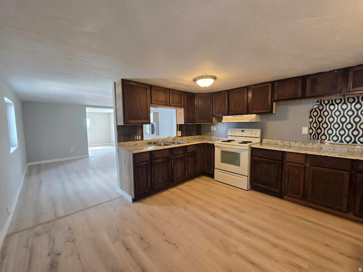 Kitchen featuring dark wood cabinetry, light-toned countertops, and an electric range with overhead ventilation
