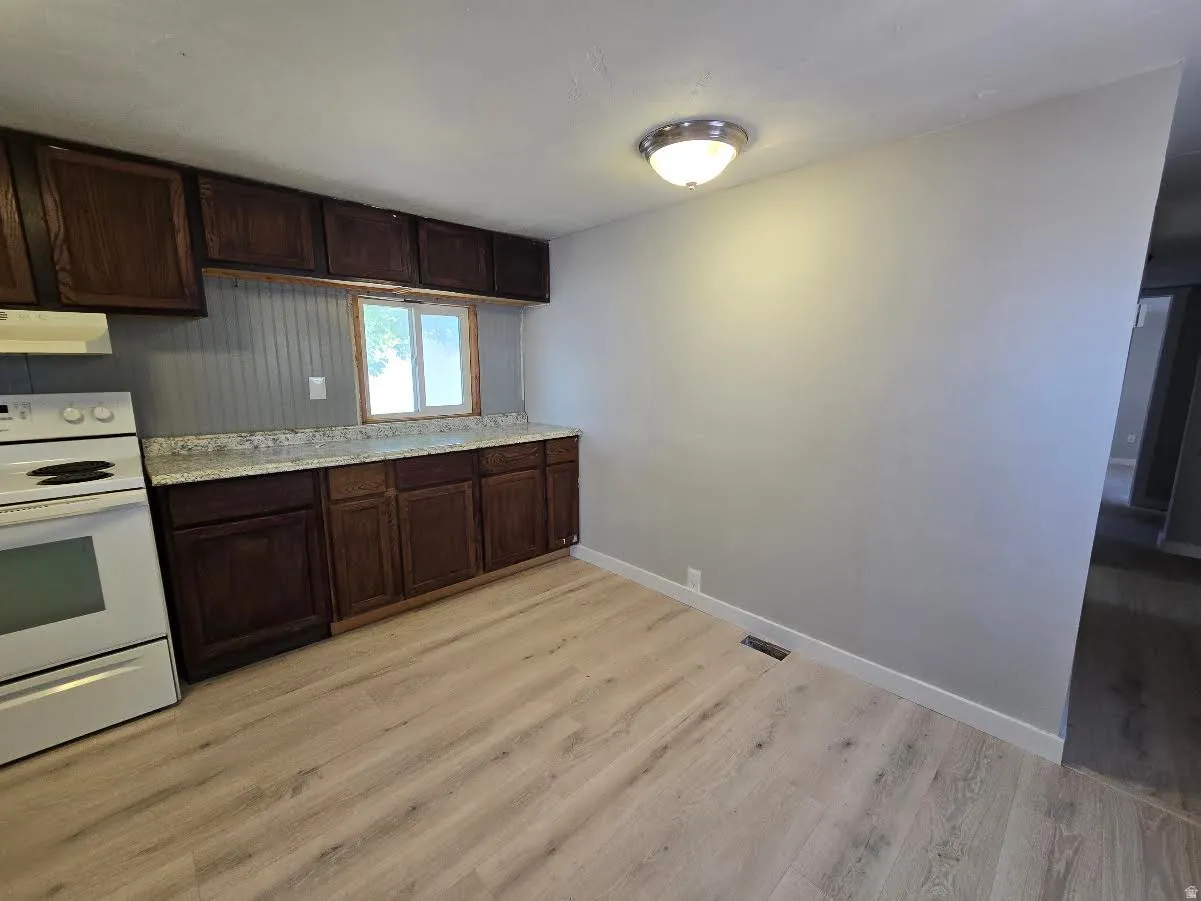 Kitchen area featuring wood-finish flooring, dark wood cabinetry, white countertops, and a white range