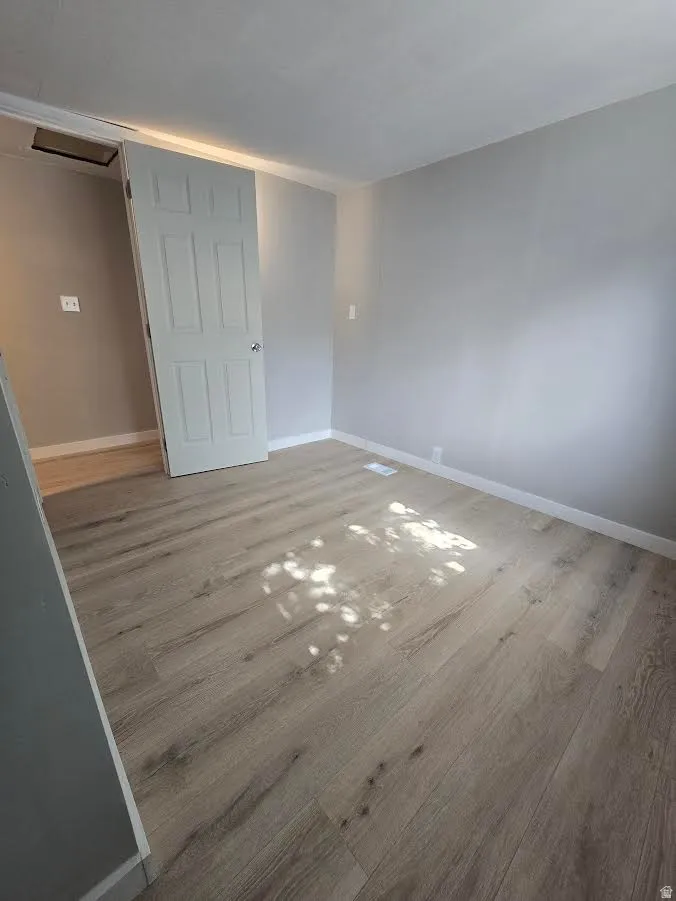 Room featuring light wood-finish flooring, light gray wall paint, white baseboards, and a white six-panel door