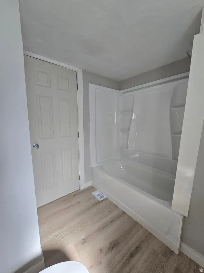Bathroom featuring a white tub and shower combination with integrated shelving, light wood-finish flooring, and a paneled white door