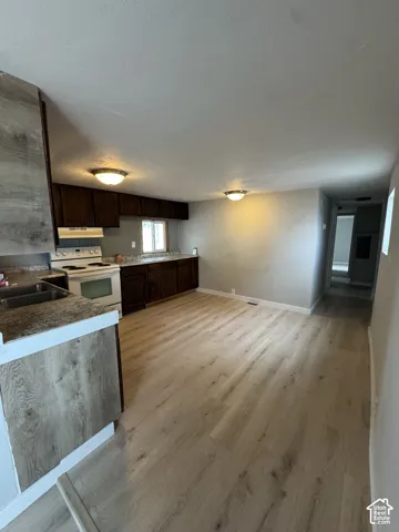 Kitchen featuring wood-finish flooring, dark-toned cabinetry, stone-patterned countertops, and dual-basin stainless steel sink