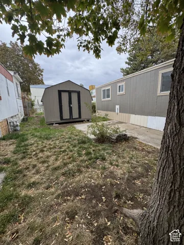 Rear exterior area featuring a detached storage shed, concrete surfacing, and mature trees