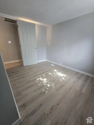 Room featuring light wood-finish flooring, light gray wall paint, white baseboards, and a white six-panel door