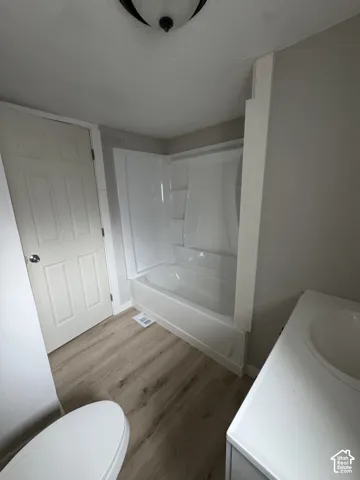 Bathroom featuring wood-finish flooring, a white composite tub surround with integrated shelving, and a single-basin vanity with a white countertop