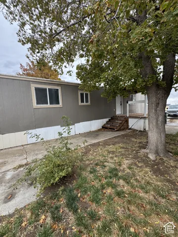 Exterior featuring a gray-toned facade, concrete driveway, elevated wood-stair entrance, and mature tree canopy
