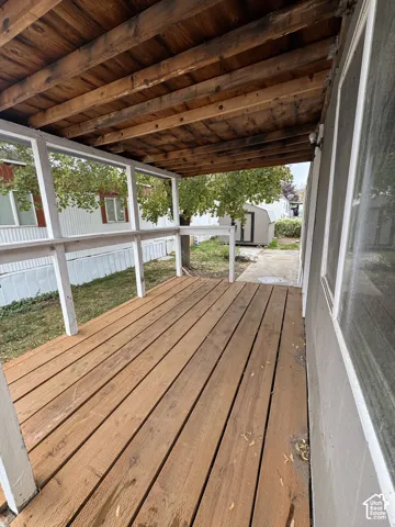 Covered wooden deck featuring exposed ceiling joists and a white wooden railing