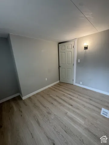 Room featuring neutral wall paint, wood-finish flooring, a six-panel door, and a wall-mounted light fixture