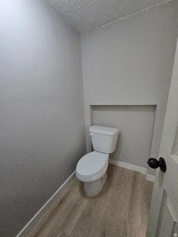 Modern water closet featuring wood-finish flooring, light grey painted walls, white baseboards, and a white toilet