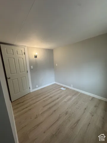 Interior space featuring wood-finish flooring, neutral wall tones, a six-panel door, and a wall-mounted light fixture