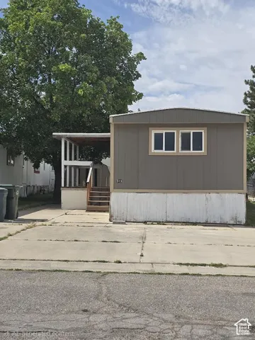 Single-story residence featuring a covered porch with white railings, a concrete driveway, and established trees providing shade