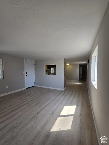 Spacious living area featuring light wood-finish flooring, neutral wall tones, and multiple windows