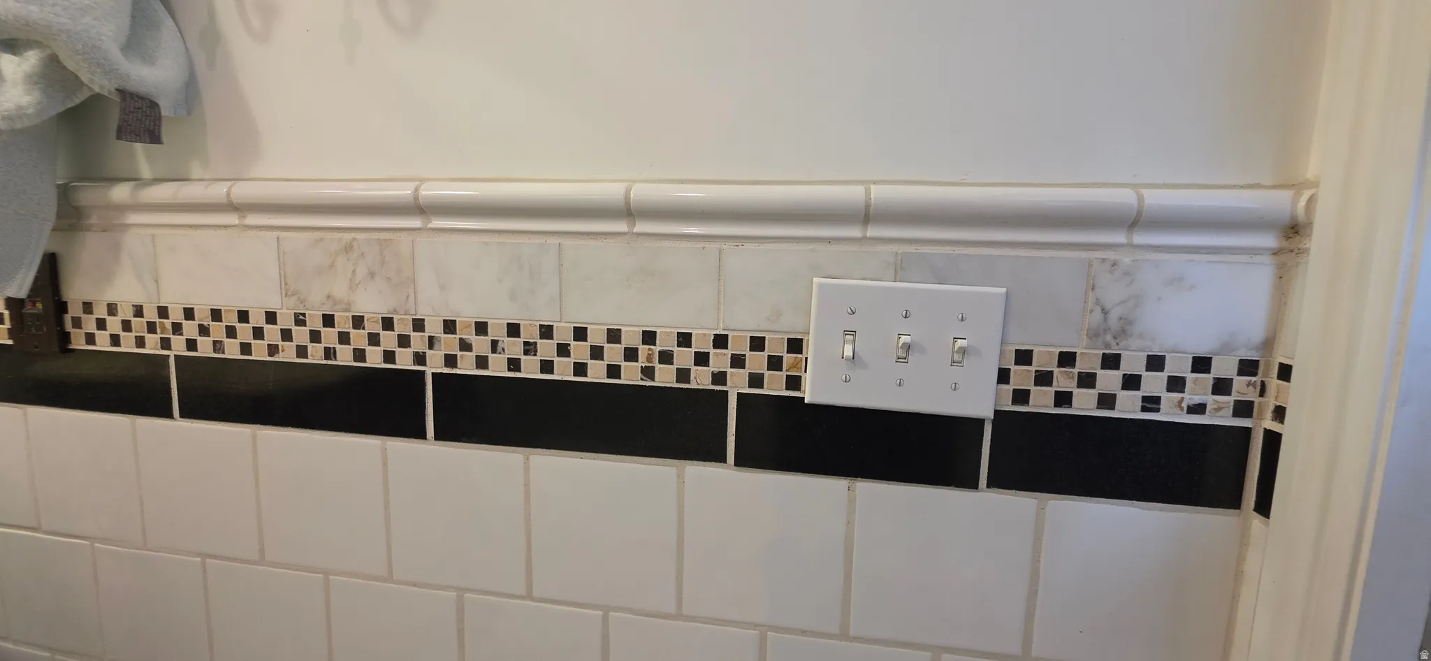 White subway tile wall with a black accent band and checkerboard mosaic trim