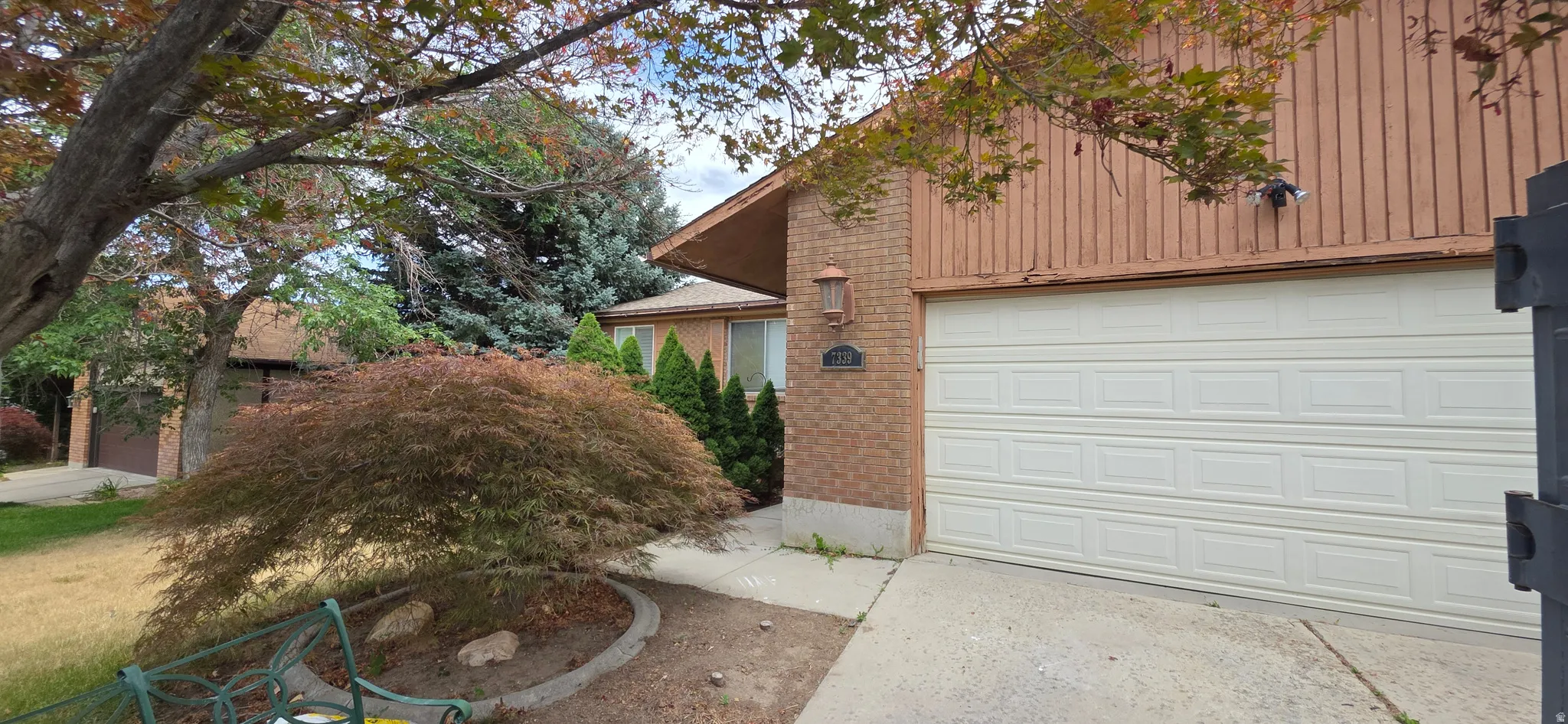 Front exterior featuring a white paneled garage door, brick facade, vertical wood siding, and mature landscaping