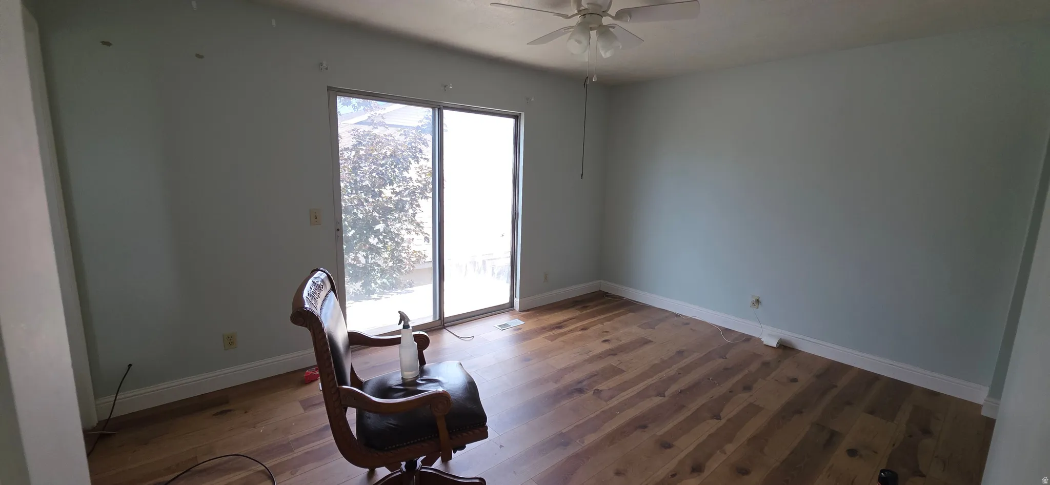Spacious room featuring wood-finish flooring, light-toned walls, and a ceiling fan