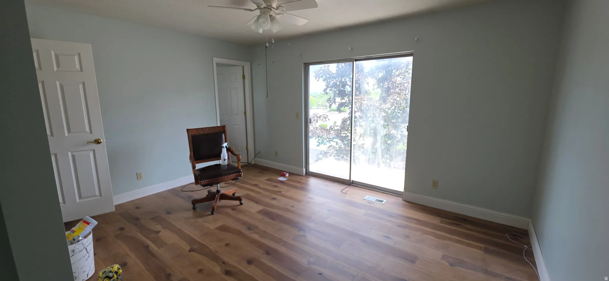 Room featuring wood-finish flooring, light blue wall finishes, white trim, and a ceiling fan