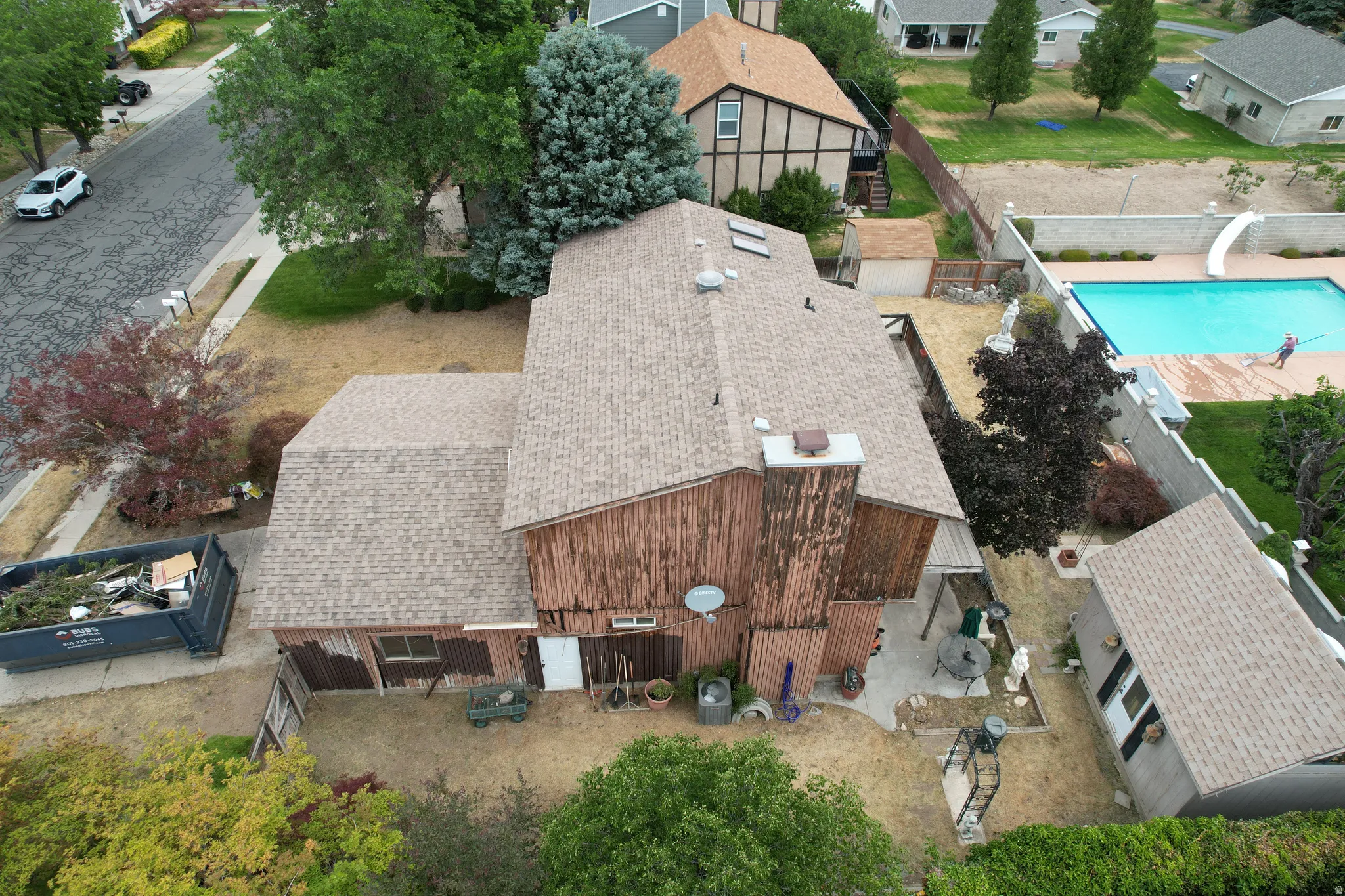 Property exterior featuring a multi-level roofline with composition shingles, a rear patio space, mature trees, and a detached shed