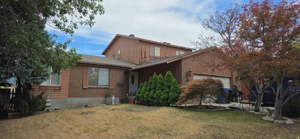 Brick and wood-sided exterior featuring a two-car garage, established front landscaping, and an inviting front entry
