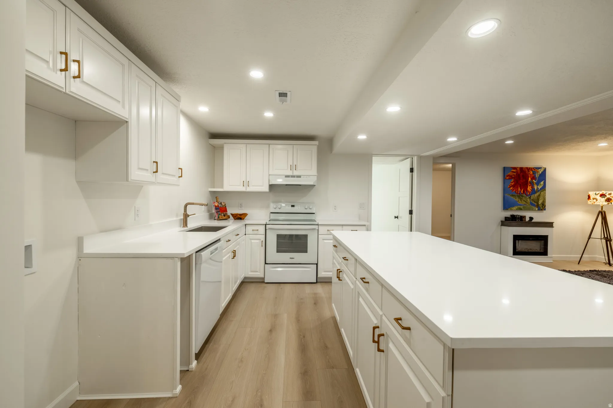 Contemporary kitchen featuring white cabinetry, bronze hardware, light-finish flooring, recessed lighting, and an extended island with a white countertop