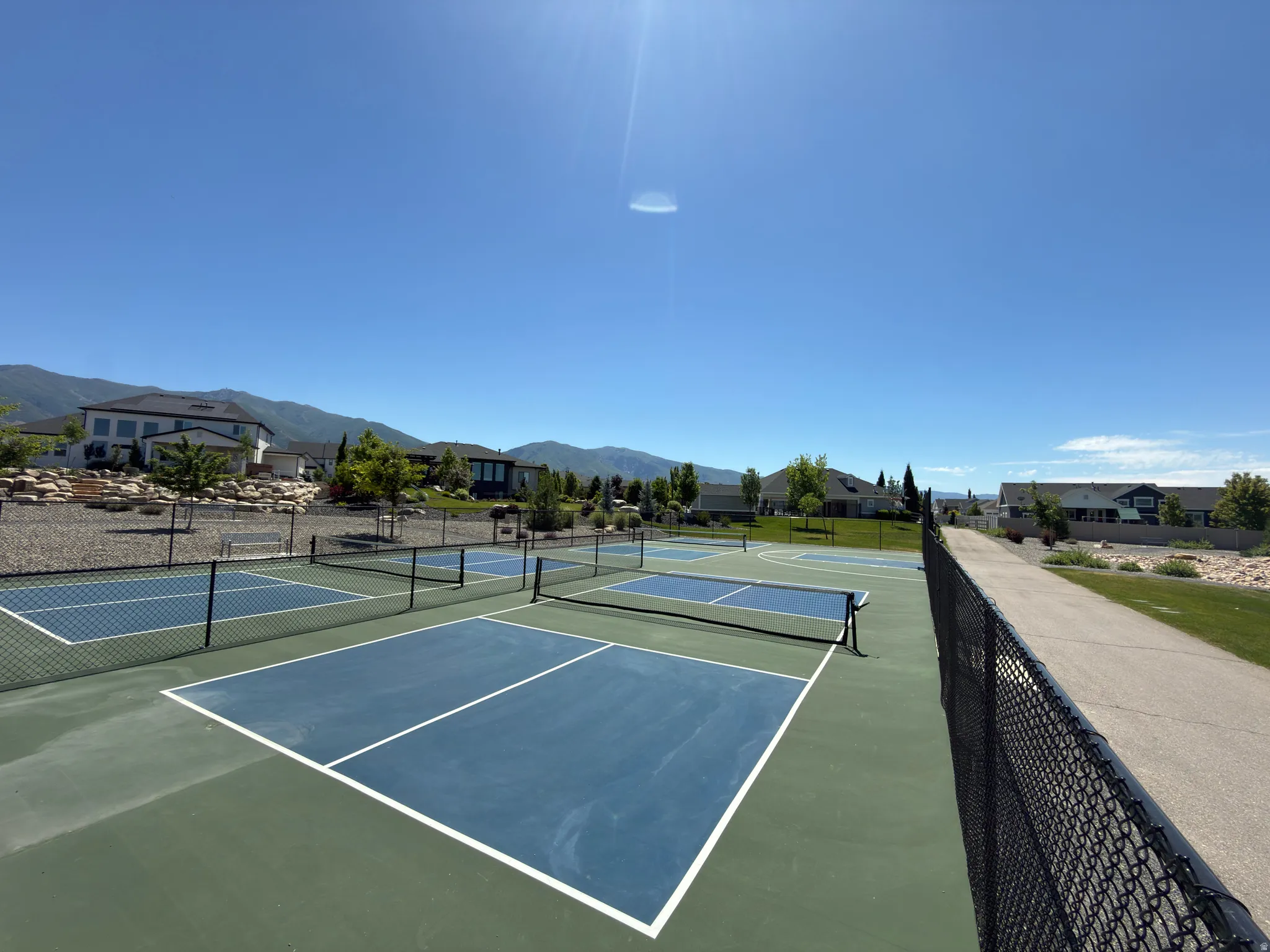 Community pickleball courts featuring multiple courts with green and blue surfaces, black chain-link fencing, and white court lines