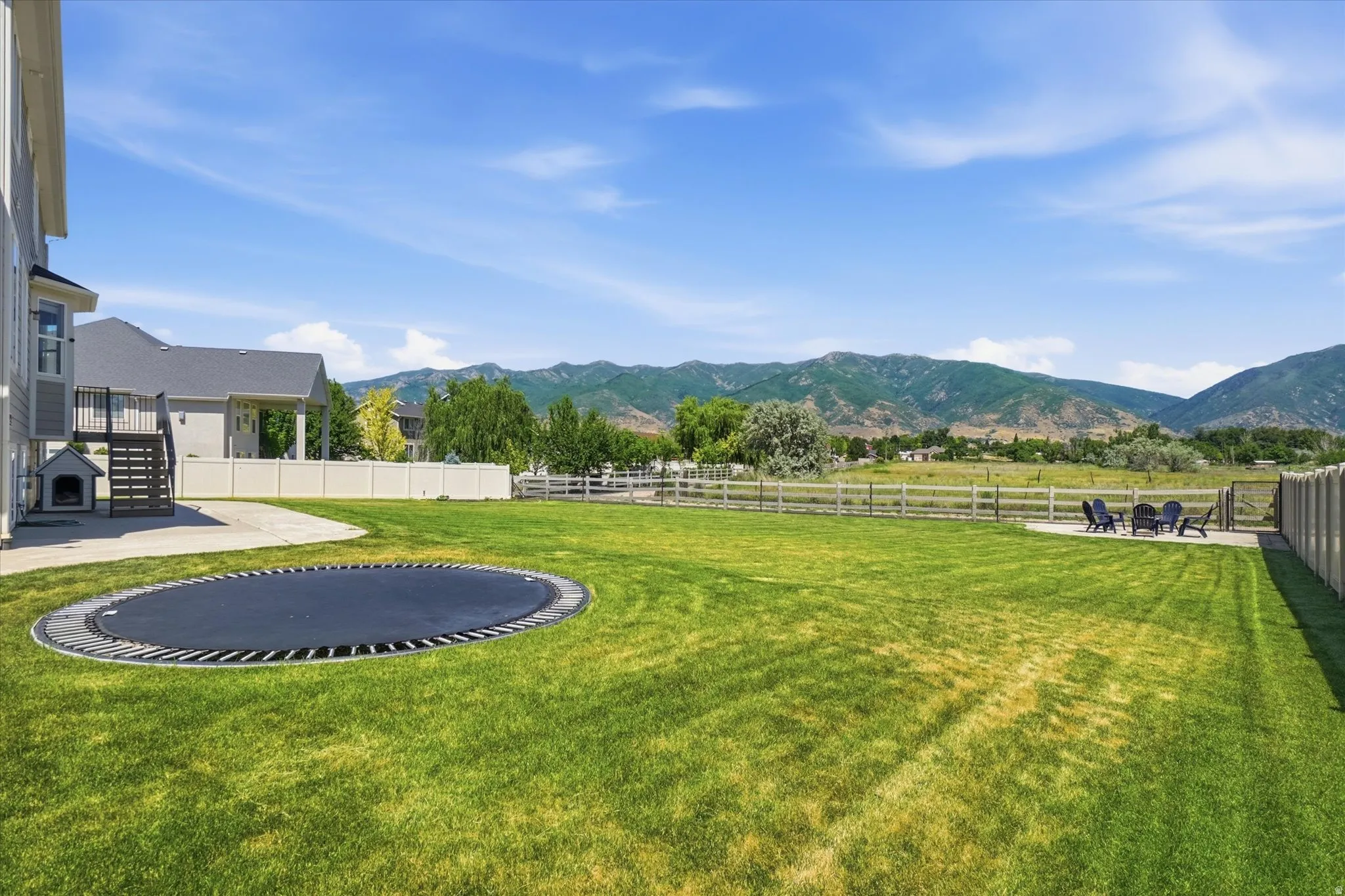 Expansive grassy yard offering mountain scenery, a concrete patio area, and an in-ground trampoline