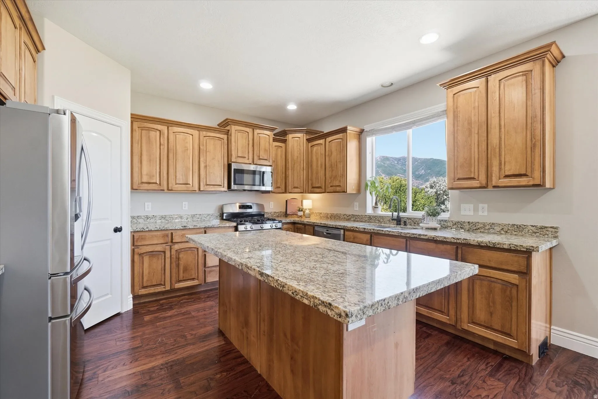 Kitchen featuring wood-finish flooring, light wood cabinetry, stone countertops, a center island with stone countertop, and stainless steel appliances