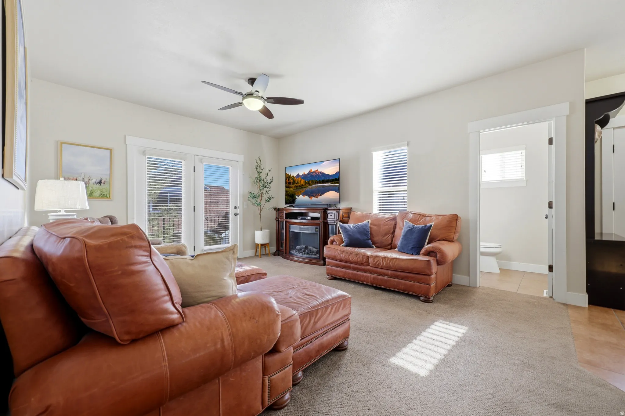 Spacious living area featuring neutral carpeting, a ceiling fan with integrated lighting, and multiple windows with blinds