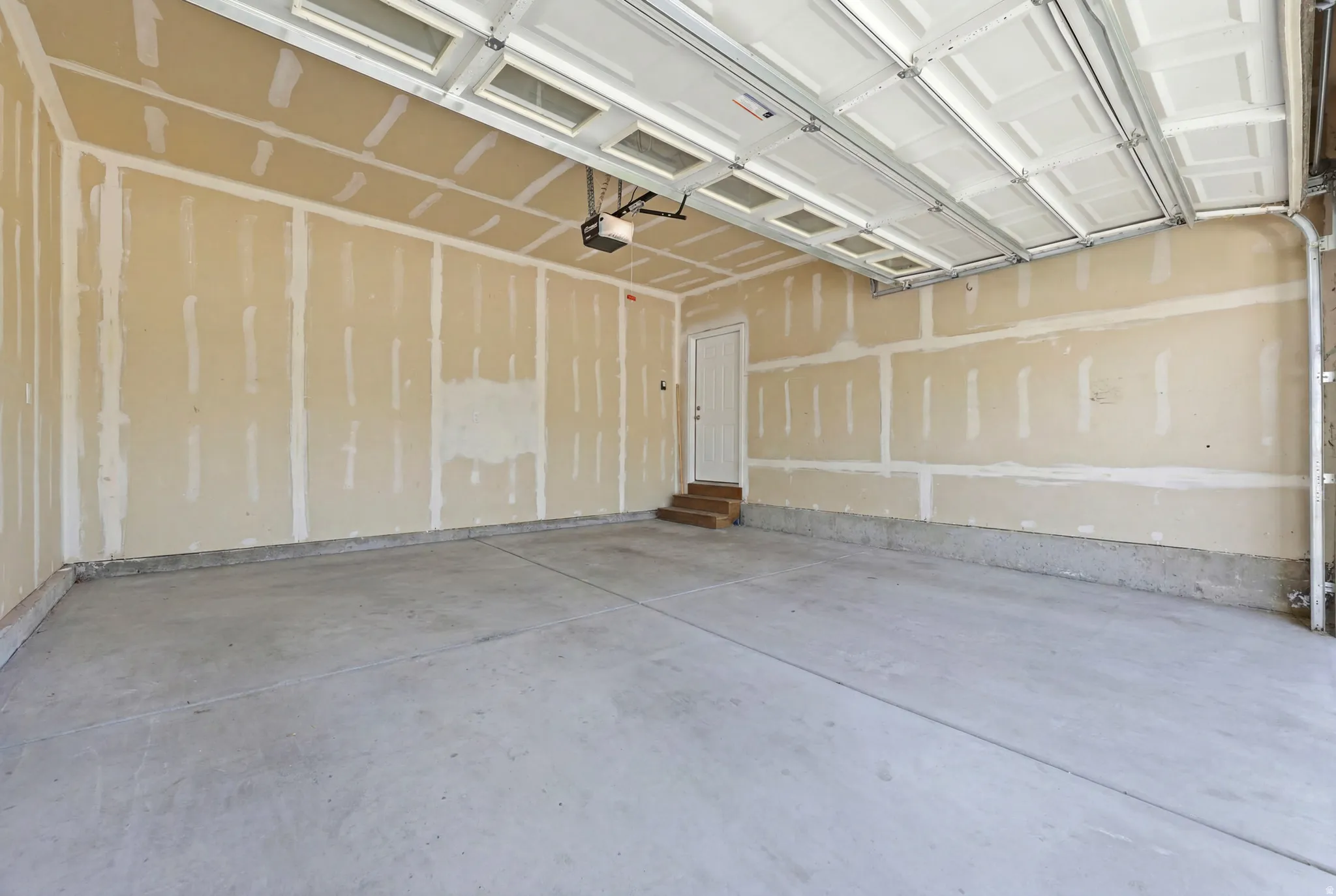 Spacious garage featuring a concrete floor, exposed drywall, and an overhead garage door