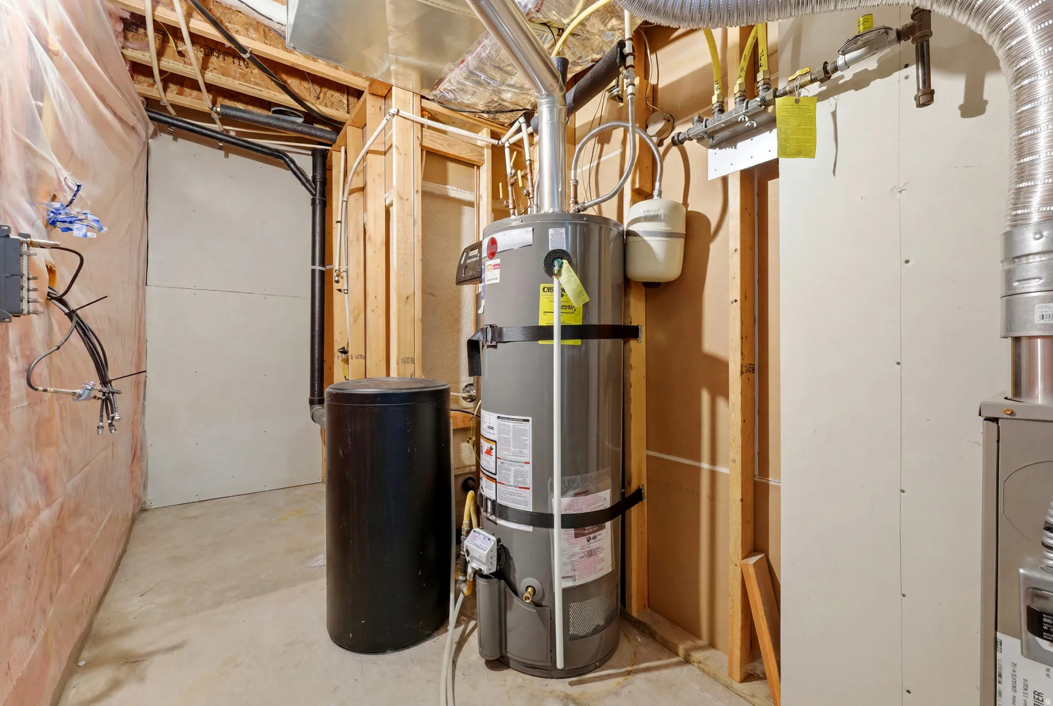 Utility area featuring a water heater, additional tank, exposed wood framing, ductwork, and concrete flooring