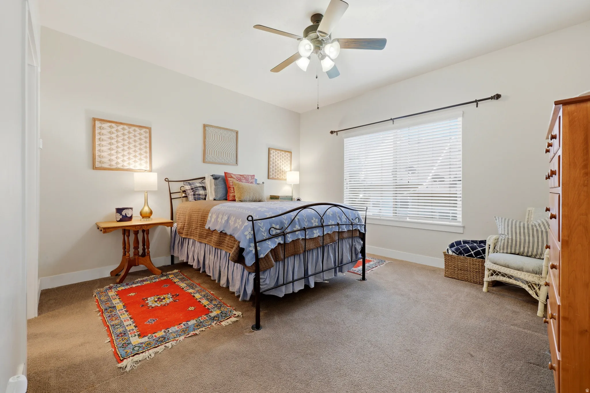 Carpeted room featuring a ceiling fan with light fixture, a large window with blinds, and white baseboards