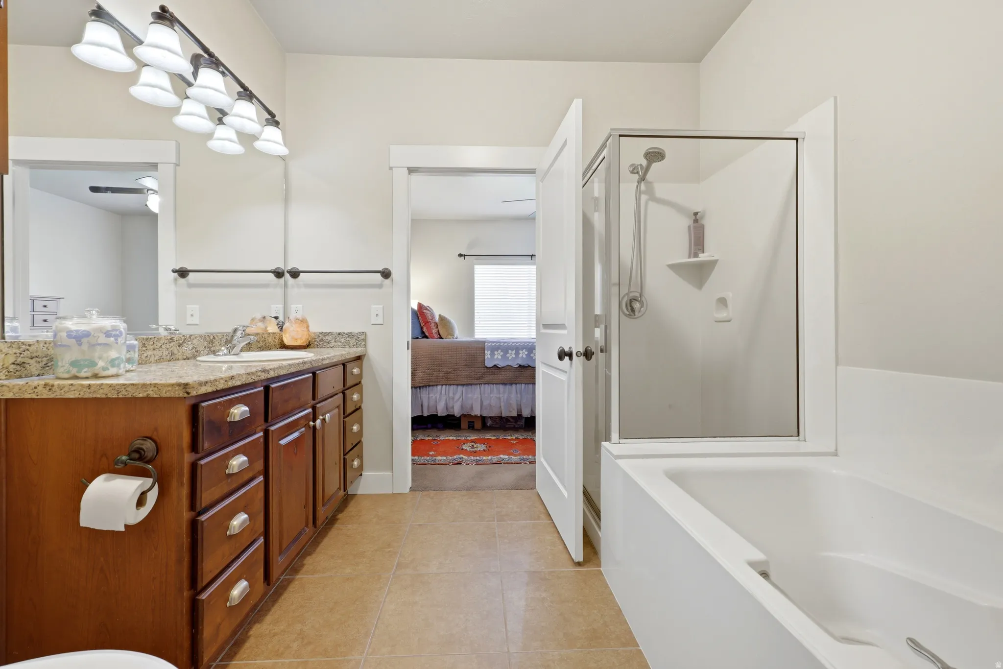 Full bathroom featuring a single vanity with a solid surface countertop, warm-toned cabinetry, a separate shower enclosure with a glass door, and a built-in soaking tub
