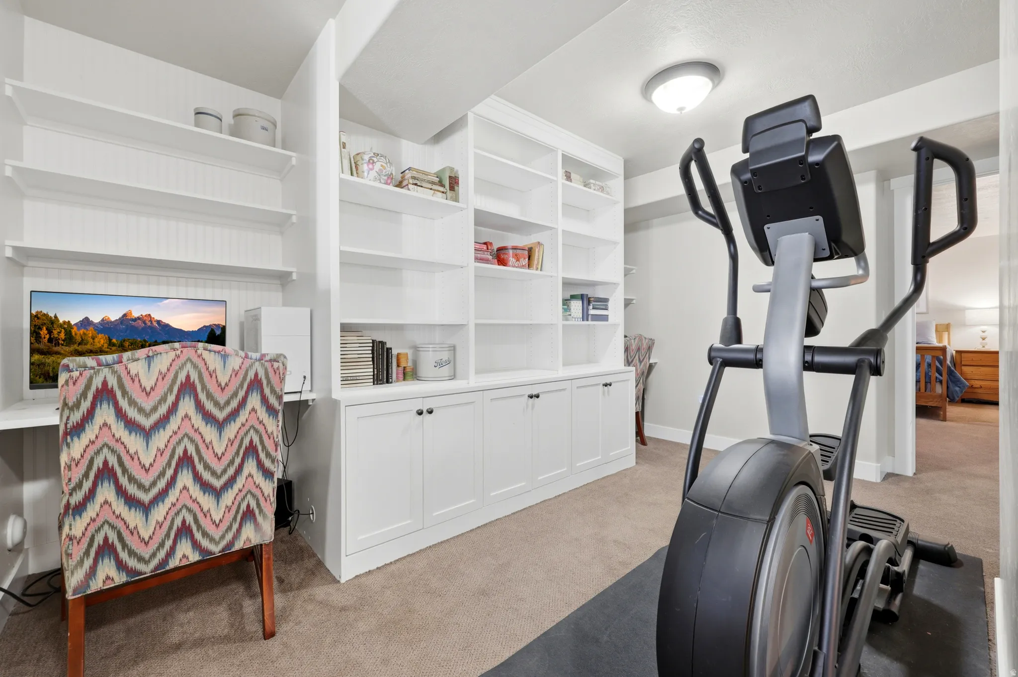 Built-in white shelving and cabinetry define this versatile space, featuring a dedicated desk area and carpeting
