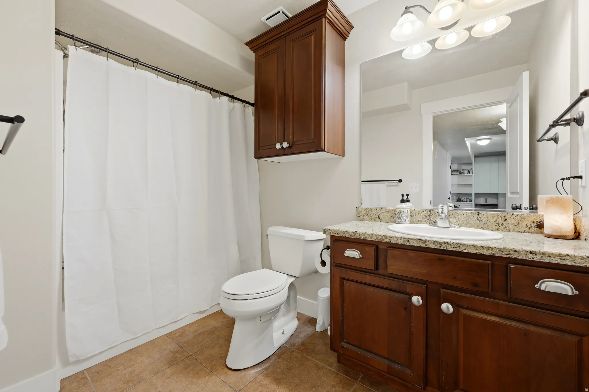 Bathroom featuring a vanity with a granite-style countertop, a single basin sink, and wood-finish cabinetry