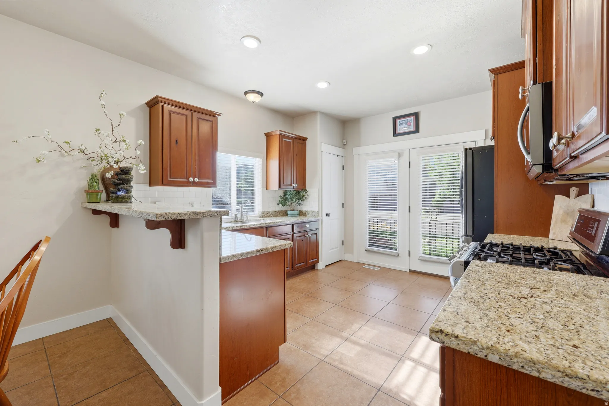 Kitchen featuring granite countertops, wood cabinetry, tile flooring, and double French doors with blinds