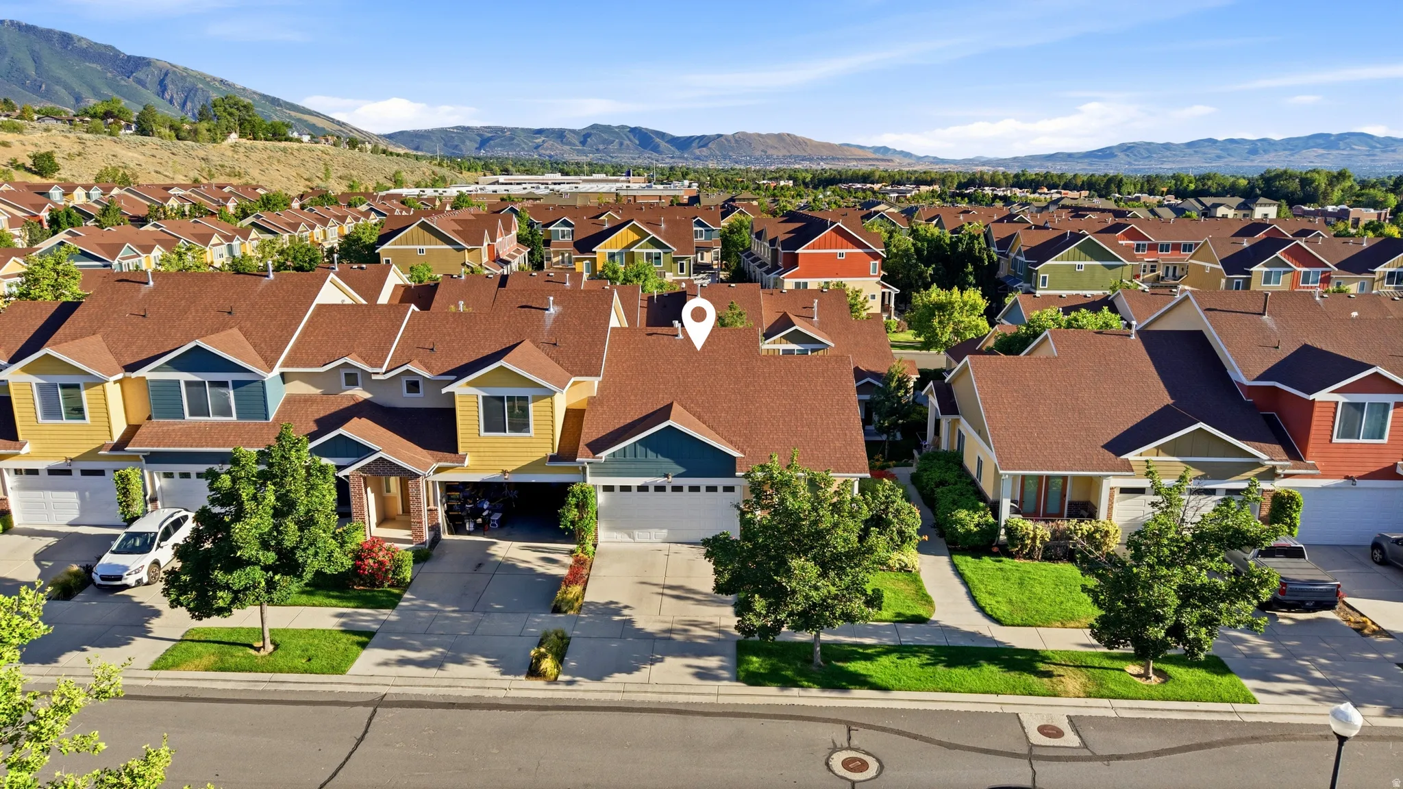 Residential property featuring a two-car garage, mature landscaping, and a mountain backdrop