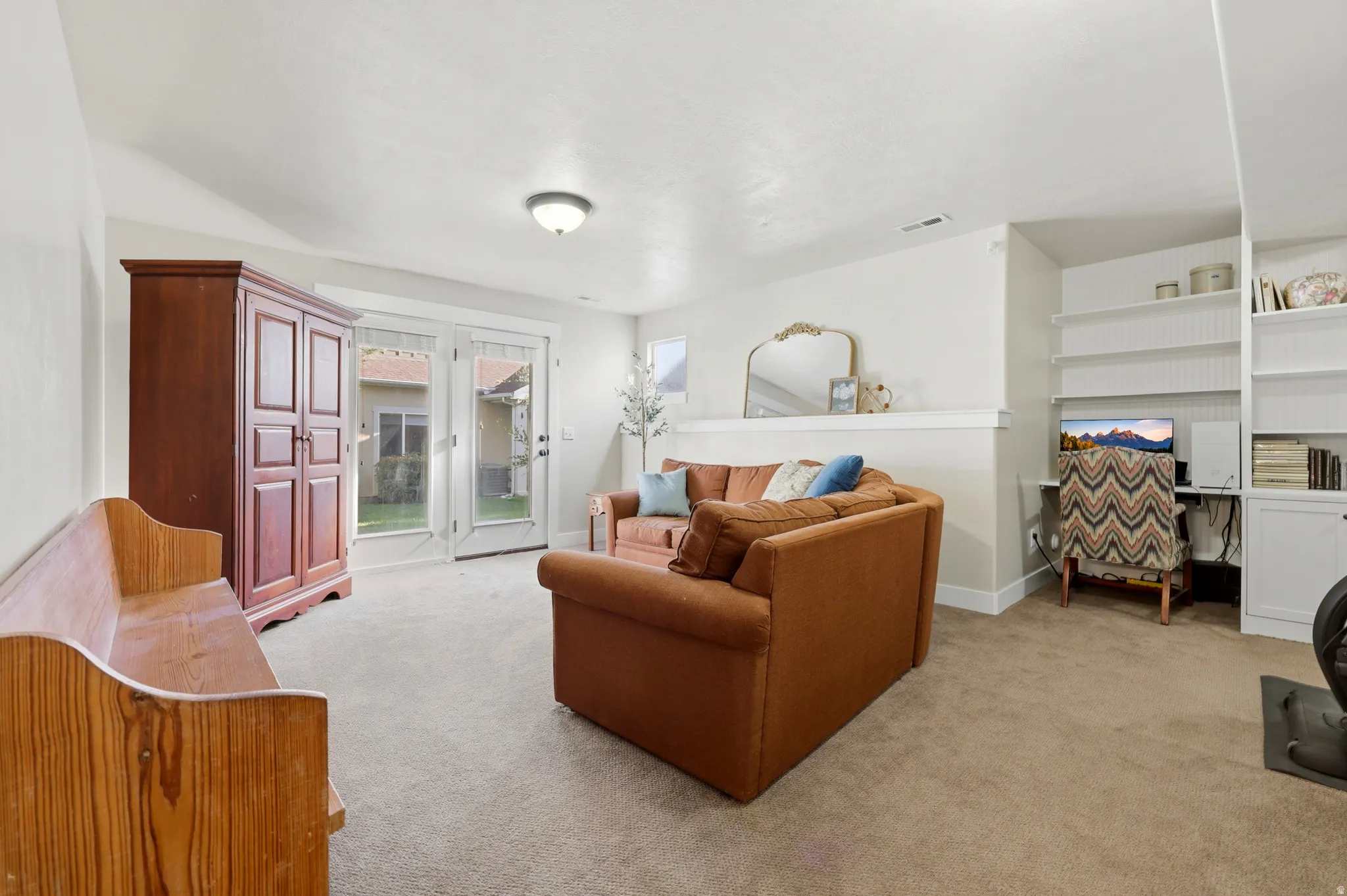 Bright living space featuring French doors, neutral carpeting, and built-in shelving with an integrated desk