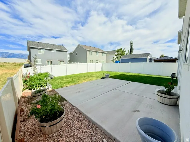 Spacious backyard featuring a concrete patio, green lawn, and white vinyl fencing