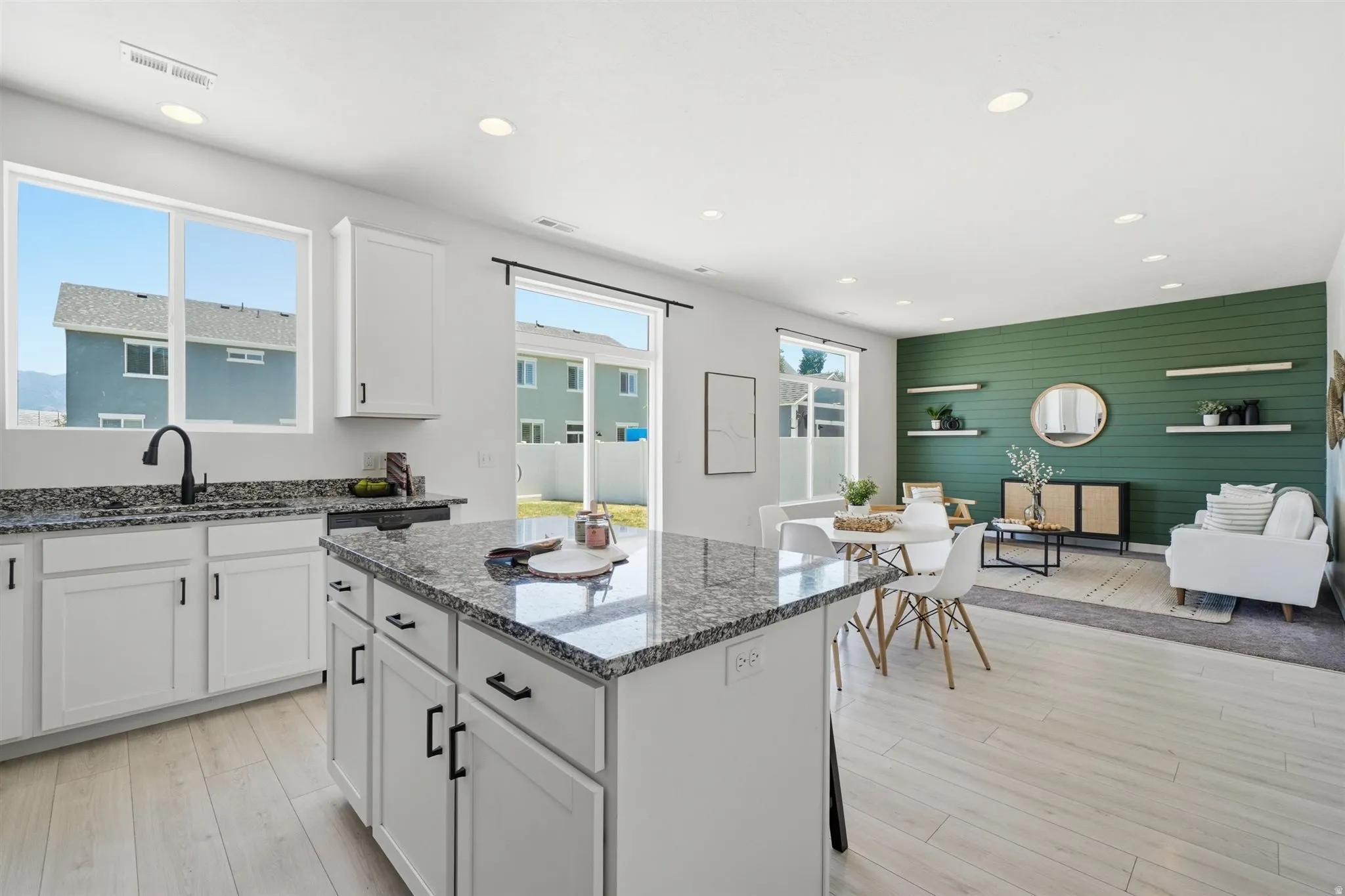 Open-concept living space featuring a kitchen island with stone-finish countertop, white cabinetry with matte black hardware, wood-finish flooring, recessed lighting, and a feature wall with shiplap detailing