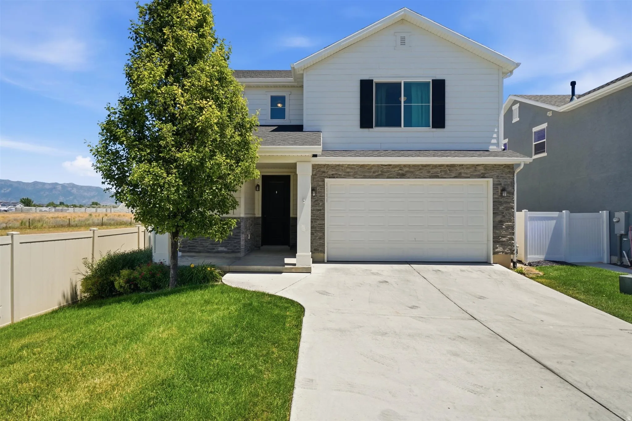 White siding exterior with stone accenting, a two-car garage, and a concrete driveway