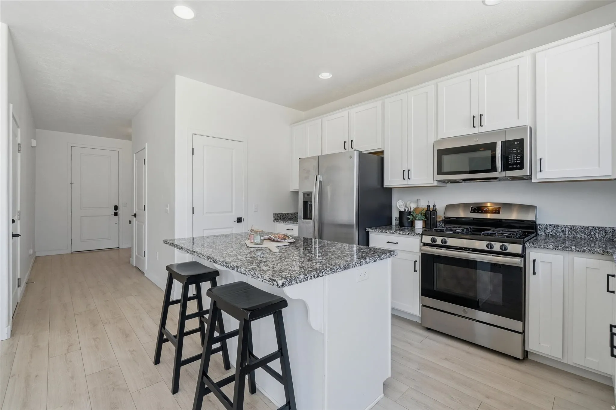 Kitchen featuring an island with seating, white shaker-style cabinetry, stainless steel appliances, granite countertops, and wood-finish flooring