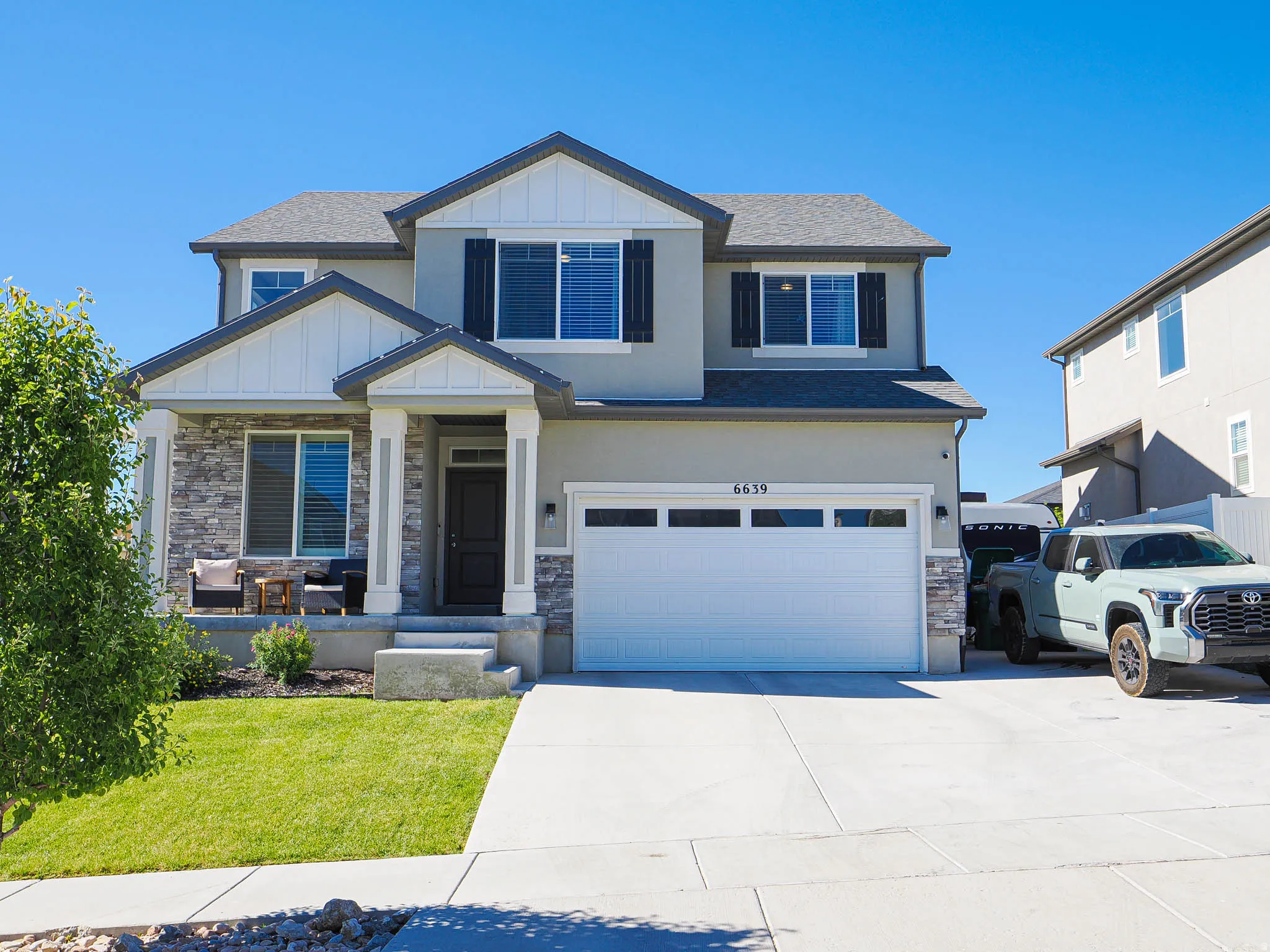 Two-story stucco and stone facade residence featuring a covered front porch, attached two-car garage, concrete driveway, and a well-maintained lawn