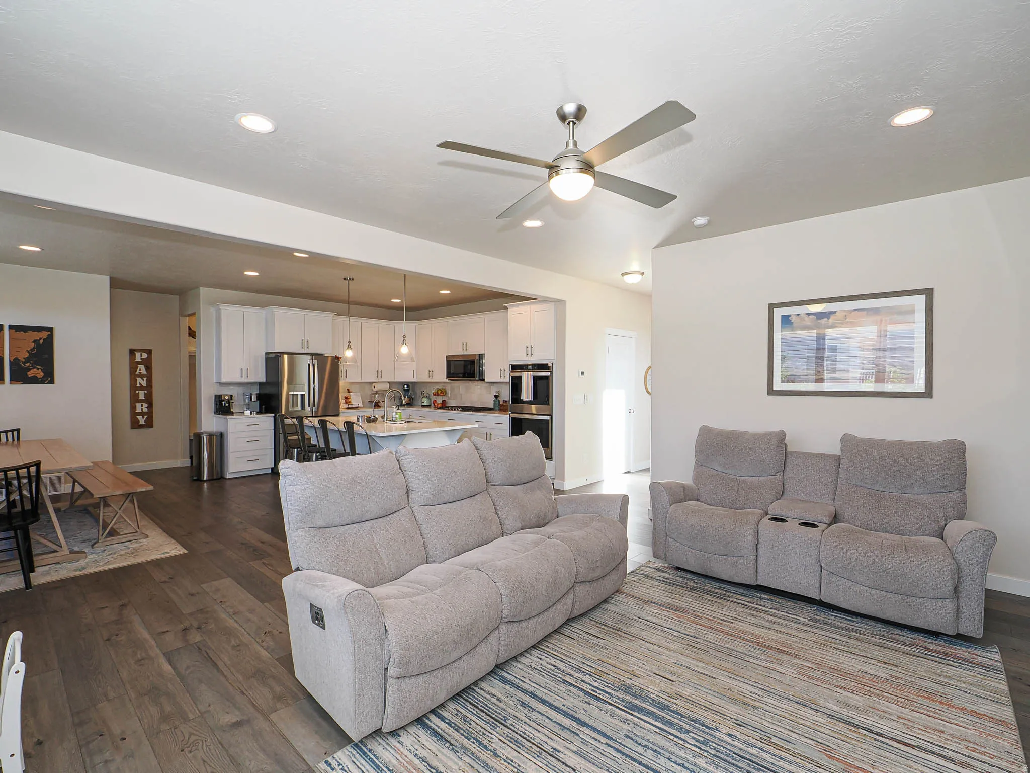 Spacious open-concept living area featuring wood-finish flooring, recessed lighting, and a vaulted ceiling with a ceiling fan