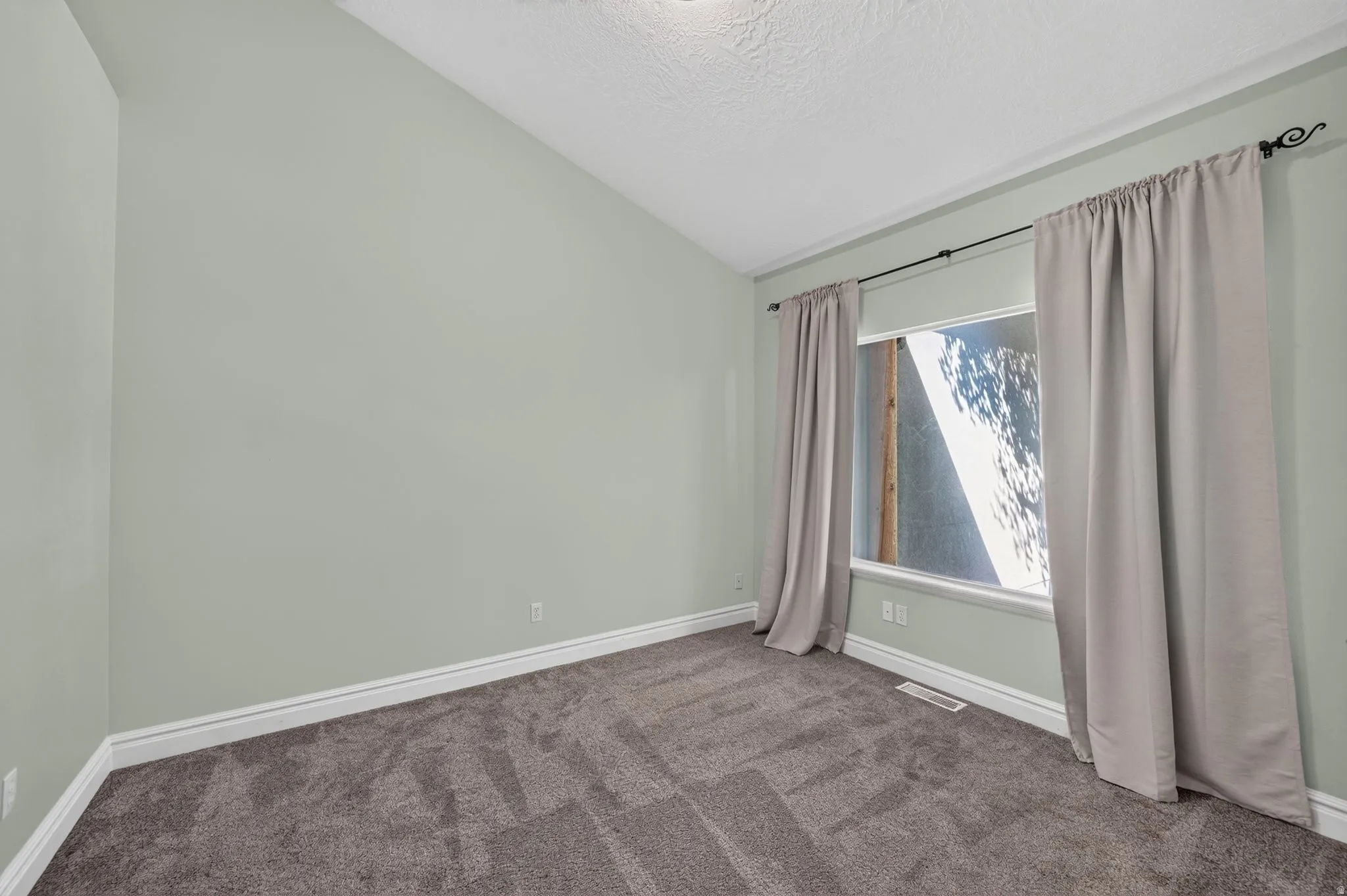 Spacious room featuring vaulted ceilings, light green walls, and plush dark gray carpeting
