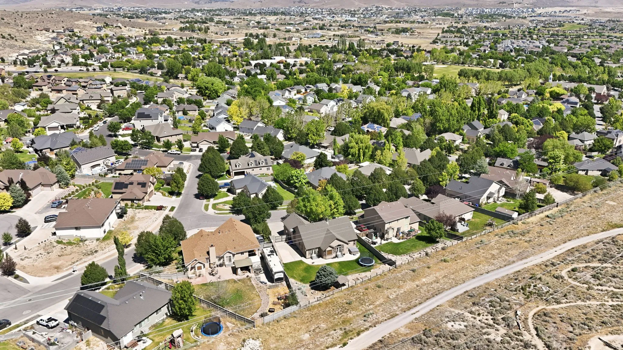 Established neighborhood featuring mature trees, paved streets, varied architectural styles, and a distant natural landscape