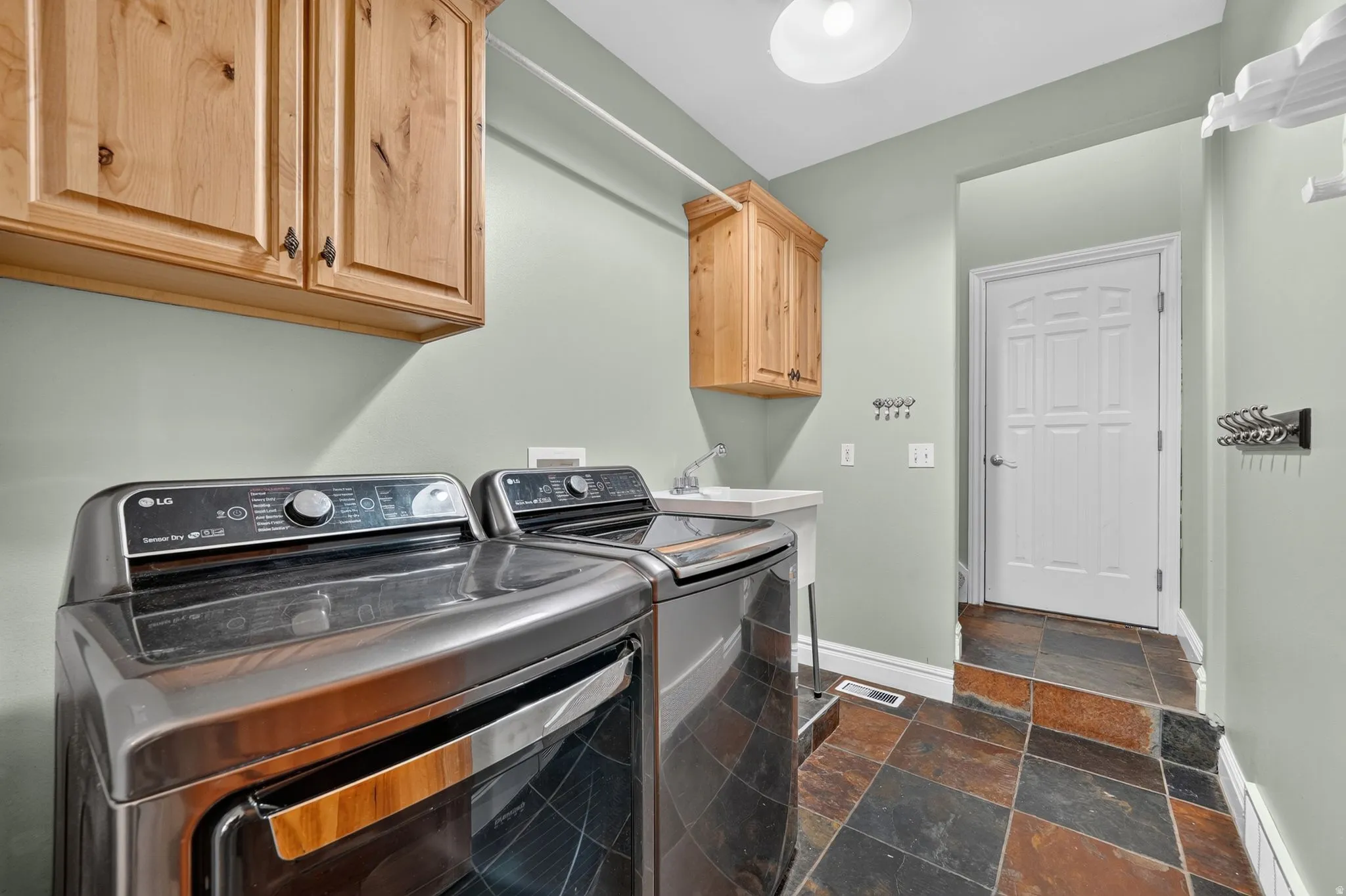 Utility room featuring wood cabinetry, a built-in utility sink, and durable slate tile flooring