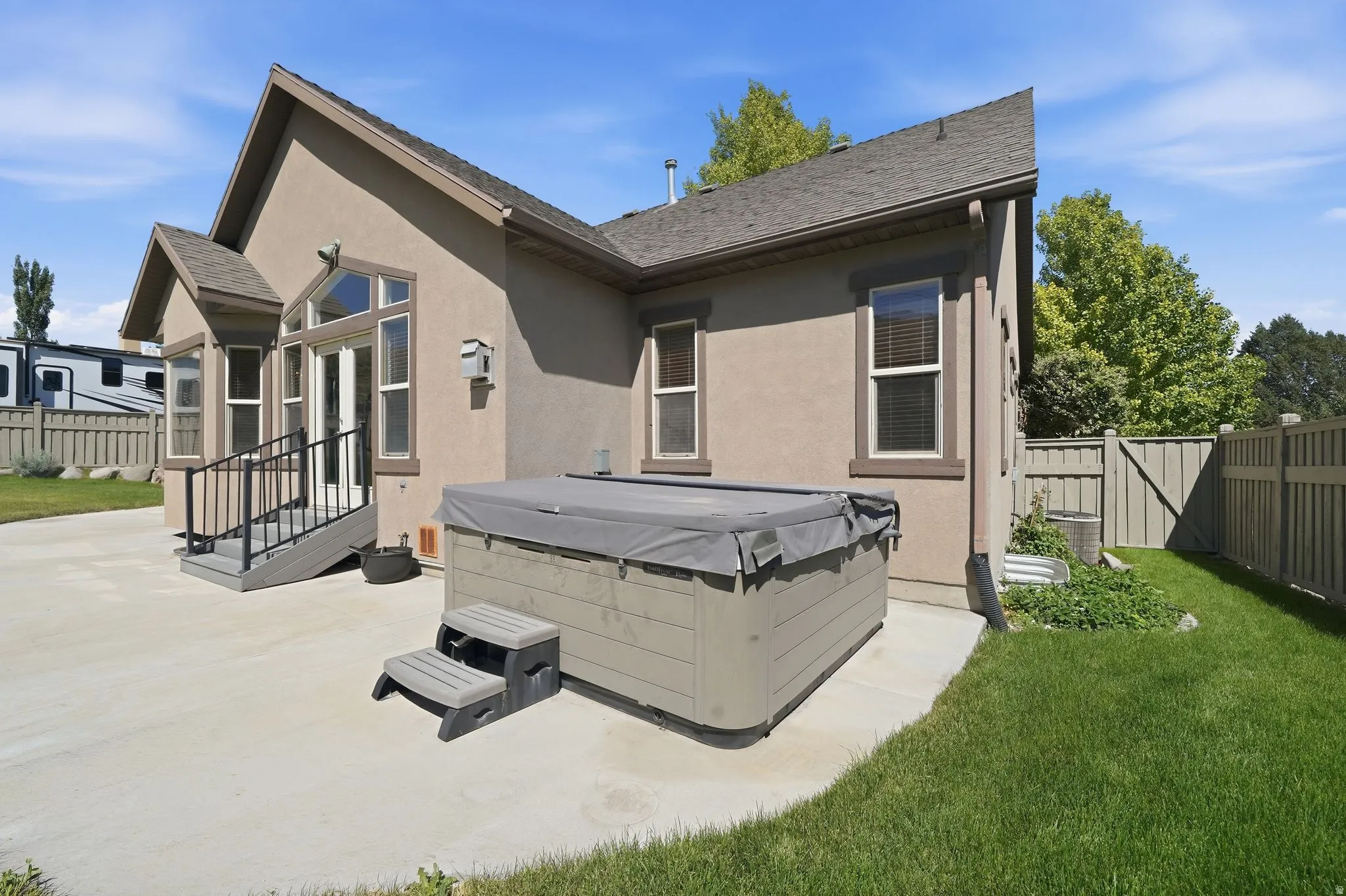 Rear exterior featuring a hot tub, concrete patio, and a staircase with black metal railings
